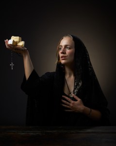 Photo of author Erika Kubick in a long black veil gazing in divine wonder at the sacred cheese cubes she holds in her hand. A rosary also dangles from the same hand.